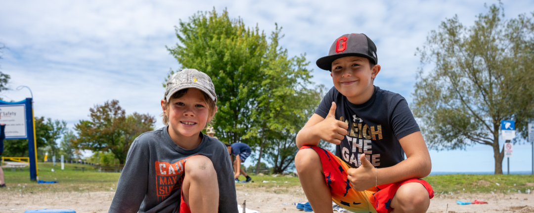 two boys playing in the sand, boy on right is giving a thumbs up
